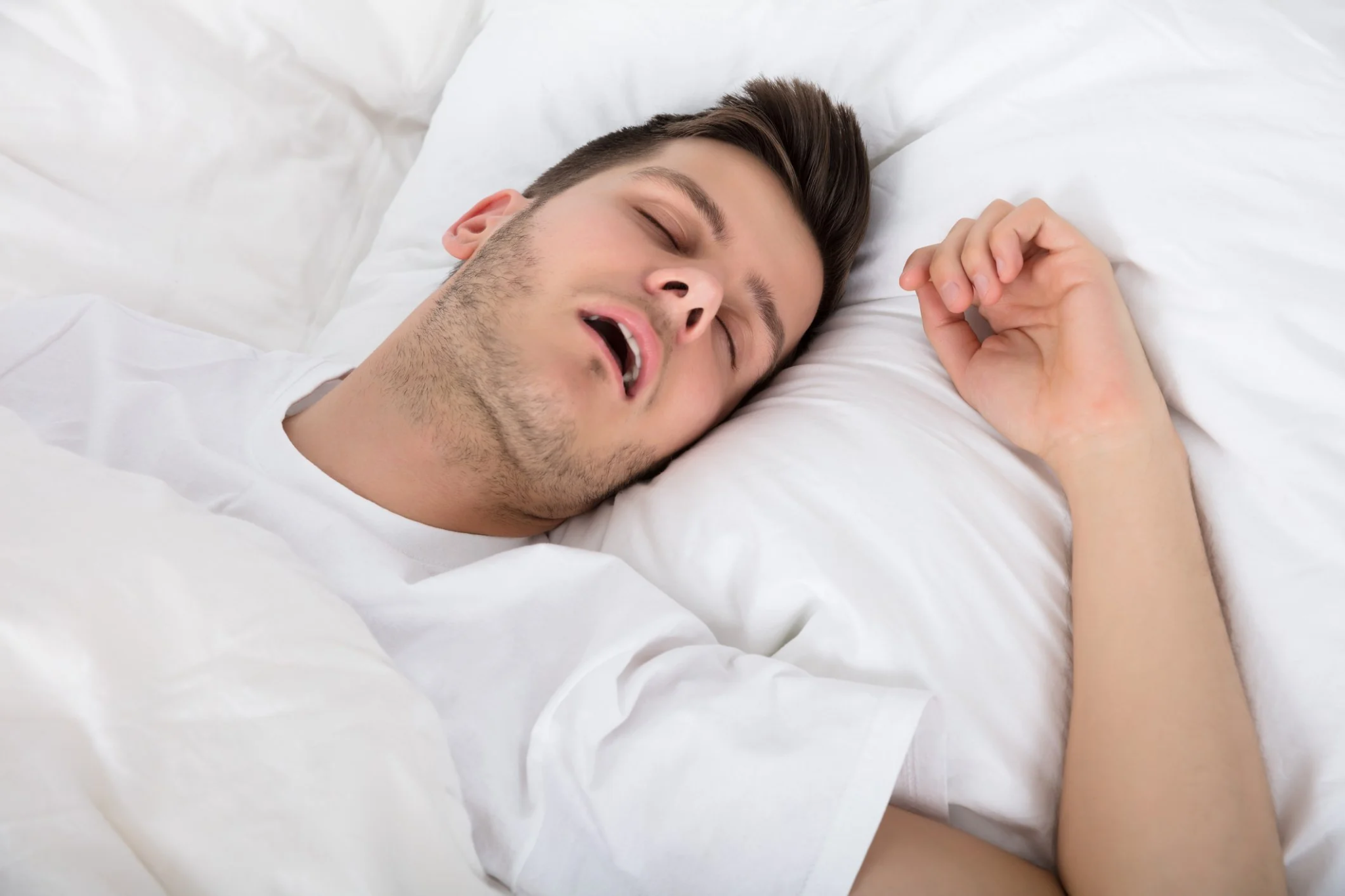Young man sleeping on white bed, head resting on pillow with eyes closed.